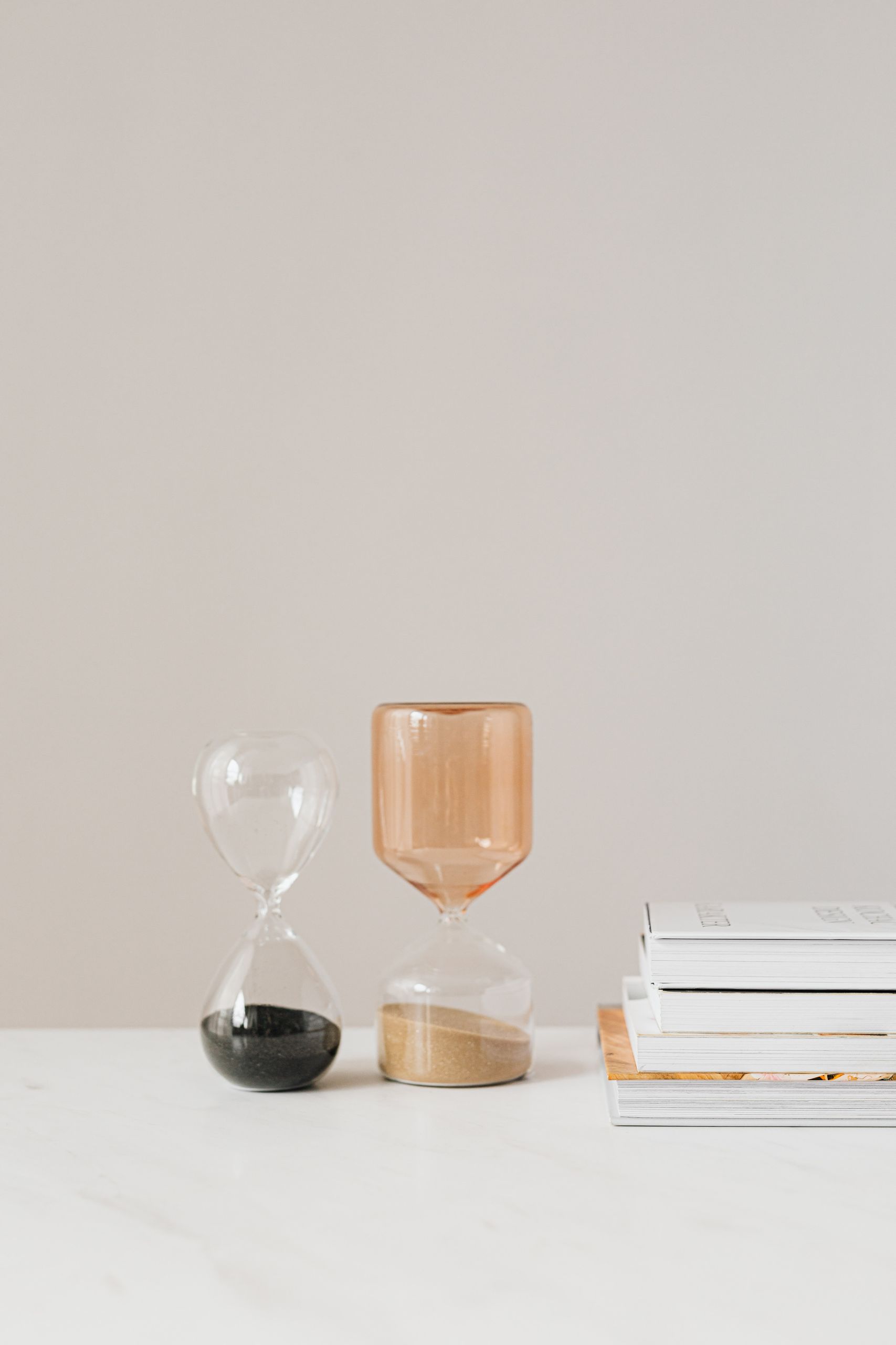 Beautiful modern hourglasses with black and rose sand on white table composed with stack of books